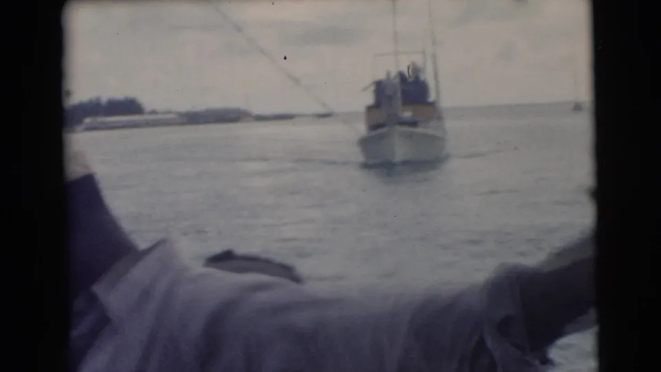 The camera catches a partial passenger view from the boat, with open water, shoreline, and another small vessel ahead.