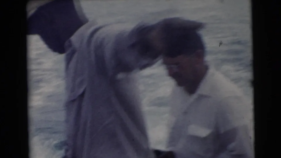 Two men appear in a soft, close boat view in 1956 Miami footage, with one bending forward near the water.
