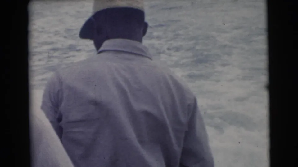 1956 Miami home-movie frame showing a man in a dark cap and light jacket facing the water from close range.