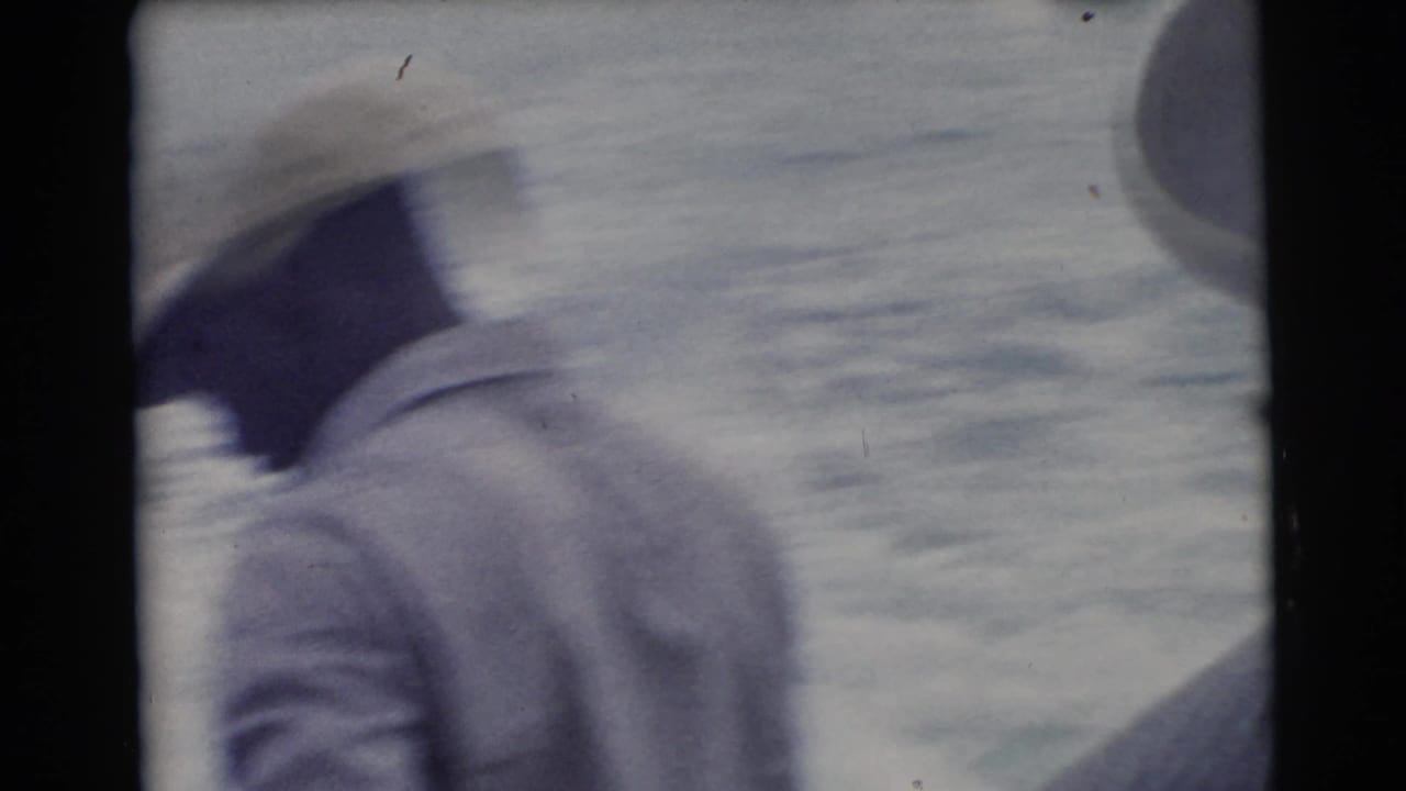Blurred man in light cap and jacket near open water.