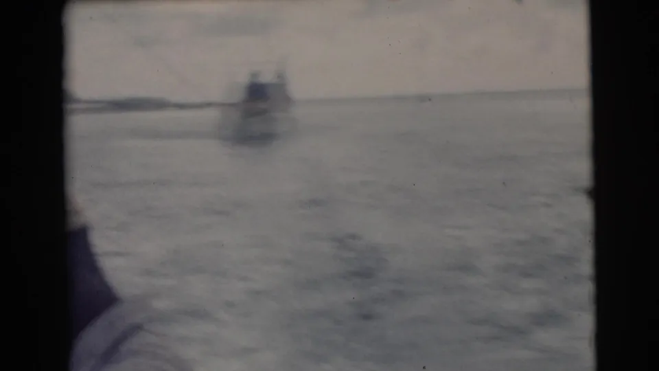Soft 8mm frame from the Miami fishing trip showing open water, a distant vessel, and a partially cropped passenger at the boat edge.