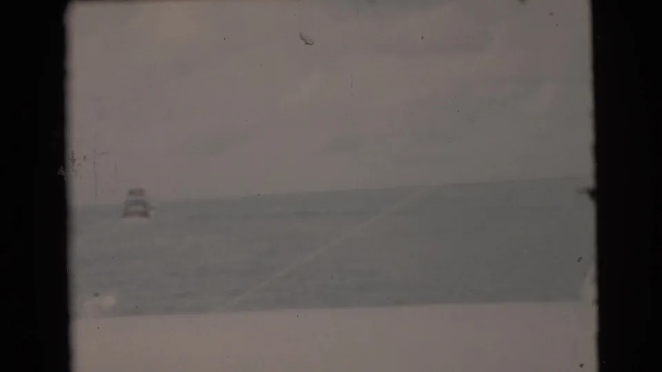 1956 Miami home-movie frame showing open water, a small distant buoy or marker, and a low horizon in muted 8mm color.