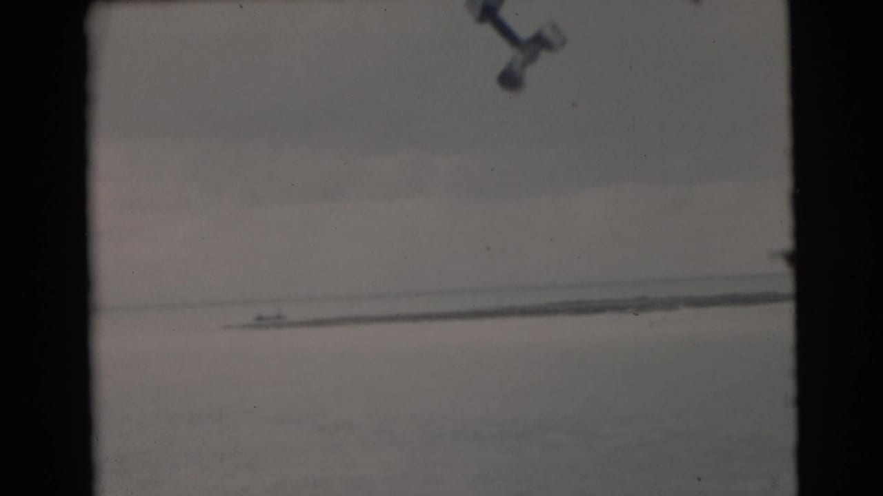 1956 Miami-area 8mm frame with a small distant boat on calm water, seen through dark vertical frame edges.