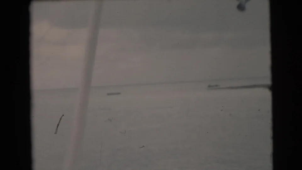 1956 Miami-area home-movie frame showing calm water, small distant boats, and dark 8mm frame or window borders.