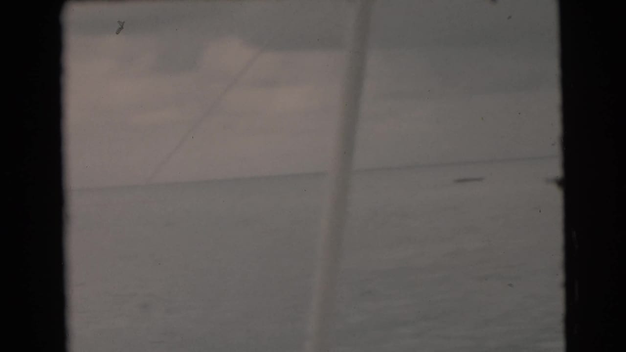 Open water and cloudy sky divided by a low horizon, with film scratches and borders visible.