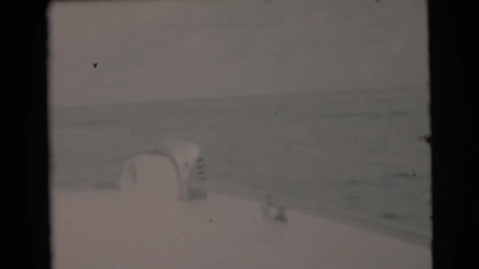 1956 Miami-area 8mm frame showing part of a boat deck or bow with a white pole, calm water, and a muted horizon beyond.