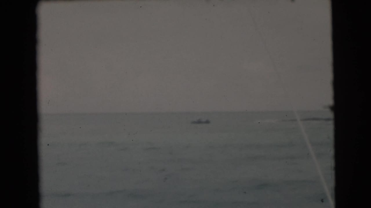 Distant small boat on choppy open water seen through a dark window frame.