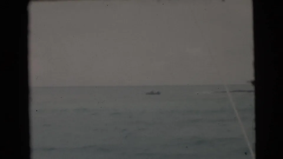 1956 Miami-area home-movie frame showing a distant boat on gray choppy water, viewed through a dark boat window frame.