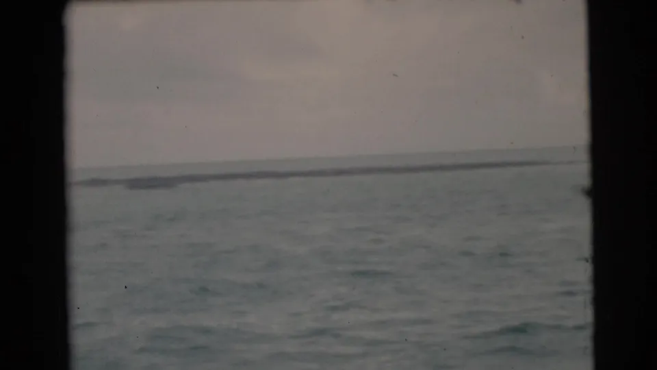 A 1956 Miami-area 8mm frame shows choppy coastal water with a low distant shoreline or vessel shape at the horizon.