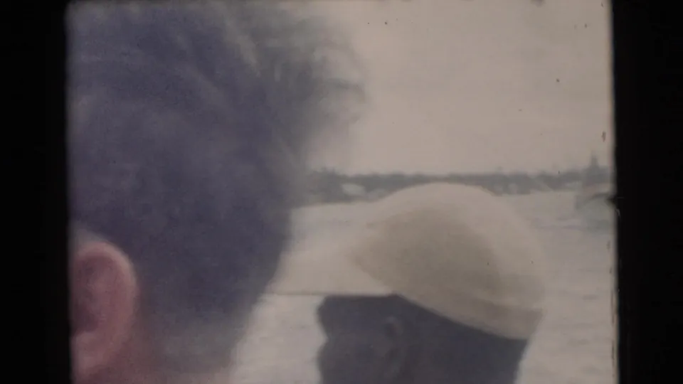 1956 Miami home-movie frame showing a man from behind on a boat, with water and shoreline beyond him.