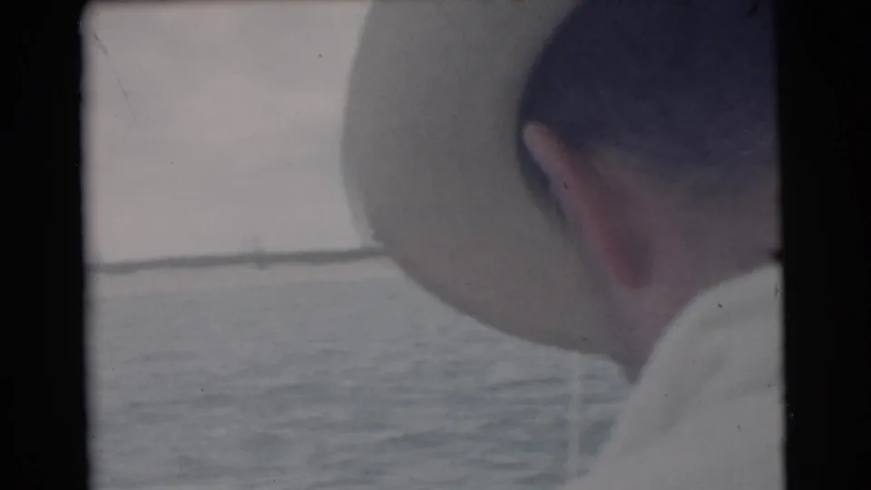 1956 Miami boat outing frame with an adult man in a light hat and sunglasses looking across the river.