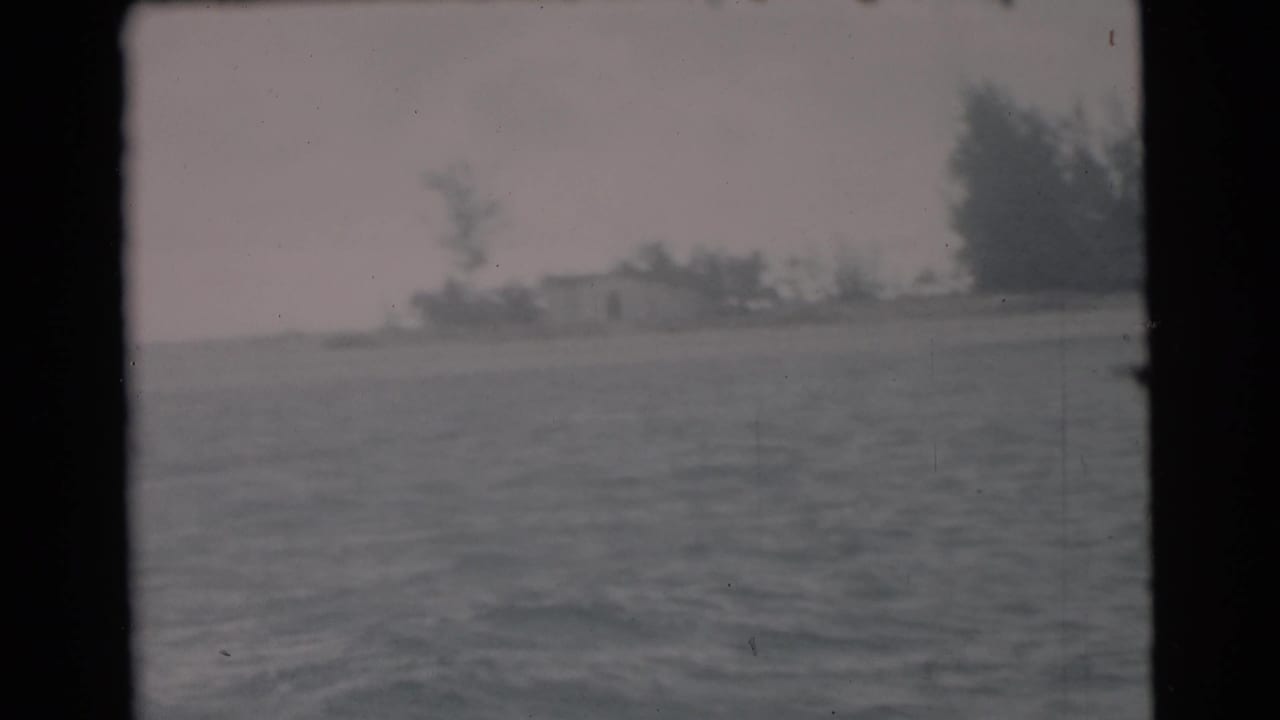 1956 Miami-area 8mm view across water toward a low shoreline with trees and small distant structures, framed by the film gate.