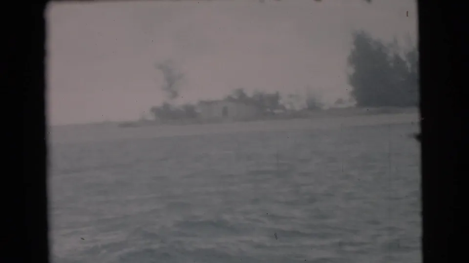 1956 Miami-area 8mm view across water toward a low shoreline with trees and small distant structures, framed by the film gate.