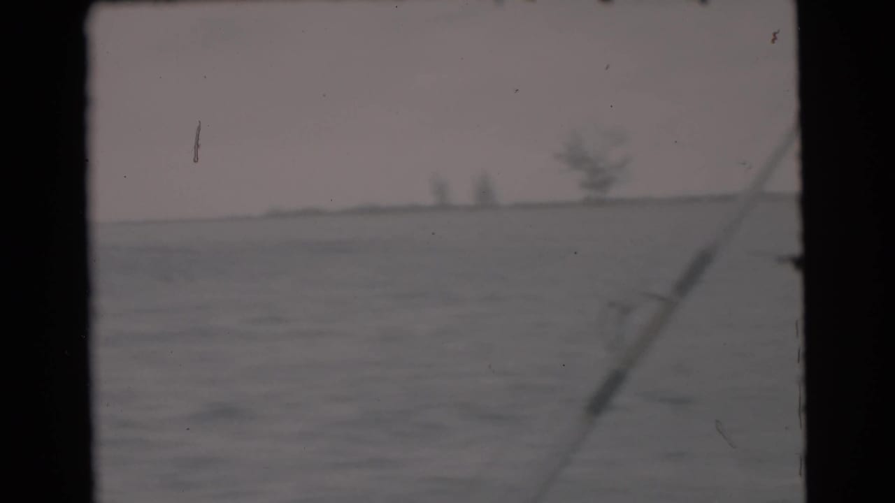 Fishing rod crossing a view of ocean with distant shoreline shapes.