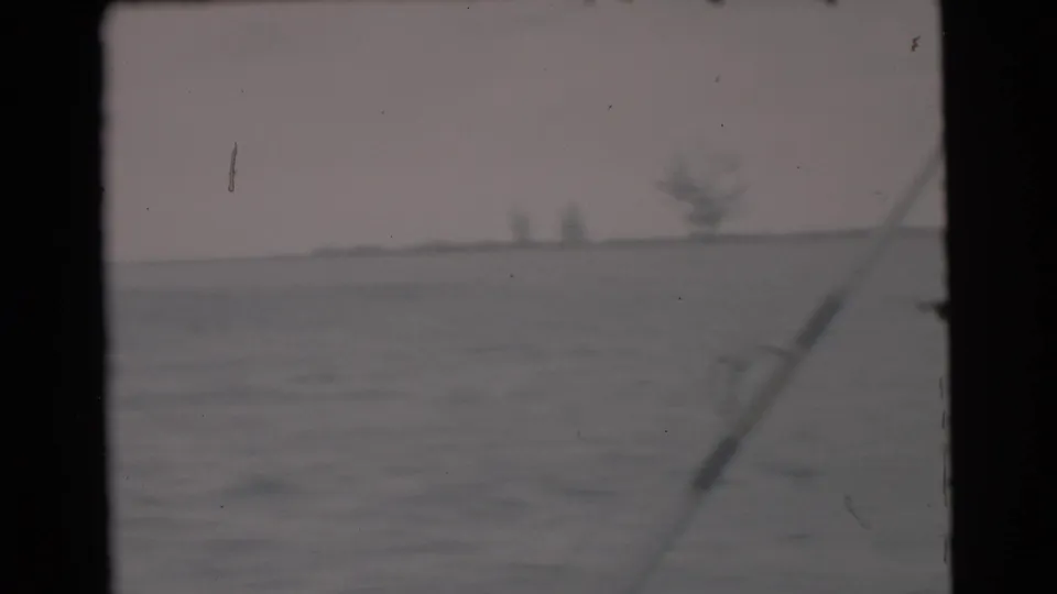 1956 Miami-area boating view with a fishing rod angled across open water and faint distant shapes on the horizon.