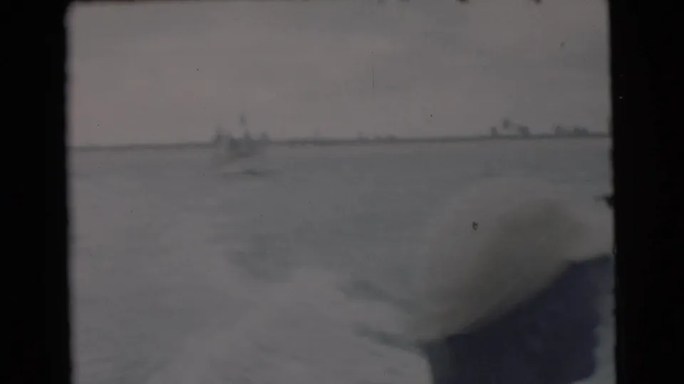1956 Miami-area 8mm frame with boat edge and wake in the foreground and distant craft or shoreline on the horizon.