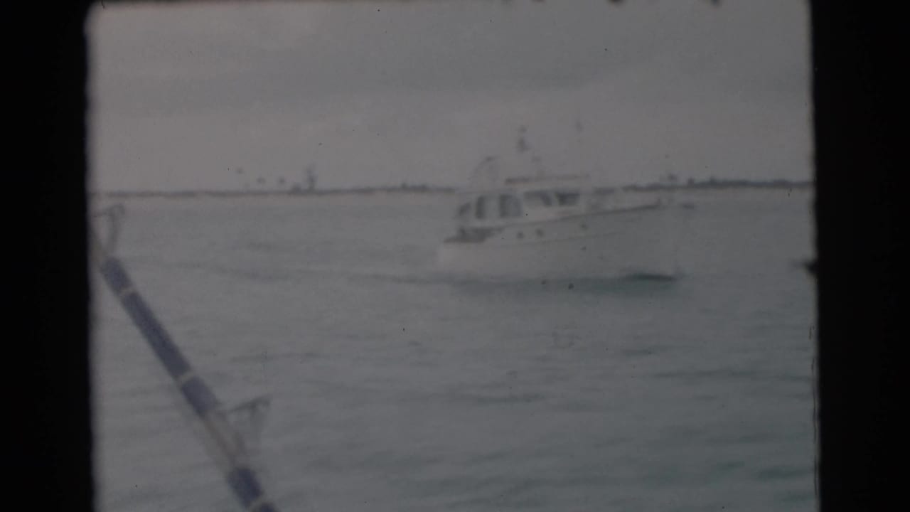White boat on choppy water with a fishing rod in the foreground.