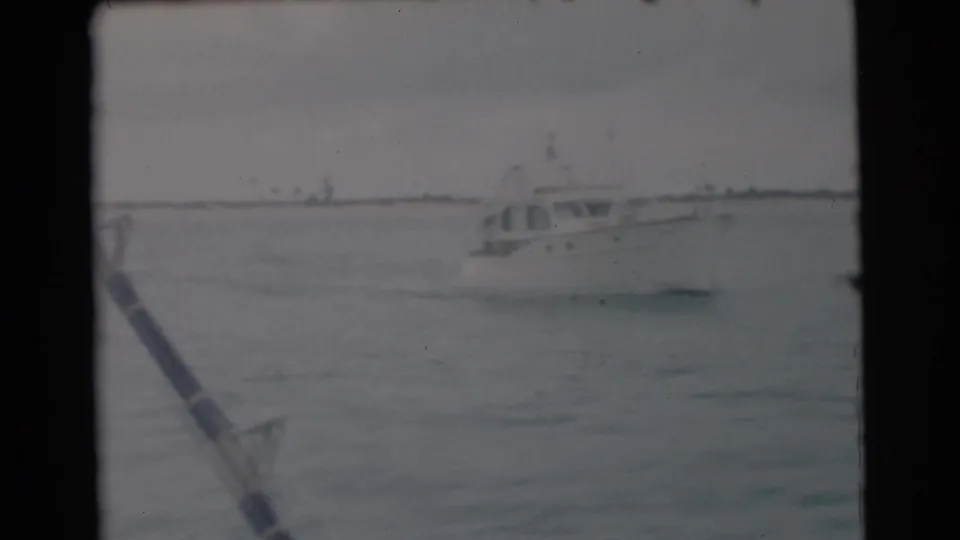 1956 Miami home-movie frame showing a white boat across choppy water with a fishing rod angled in the foreground.