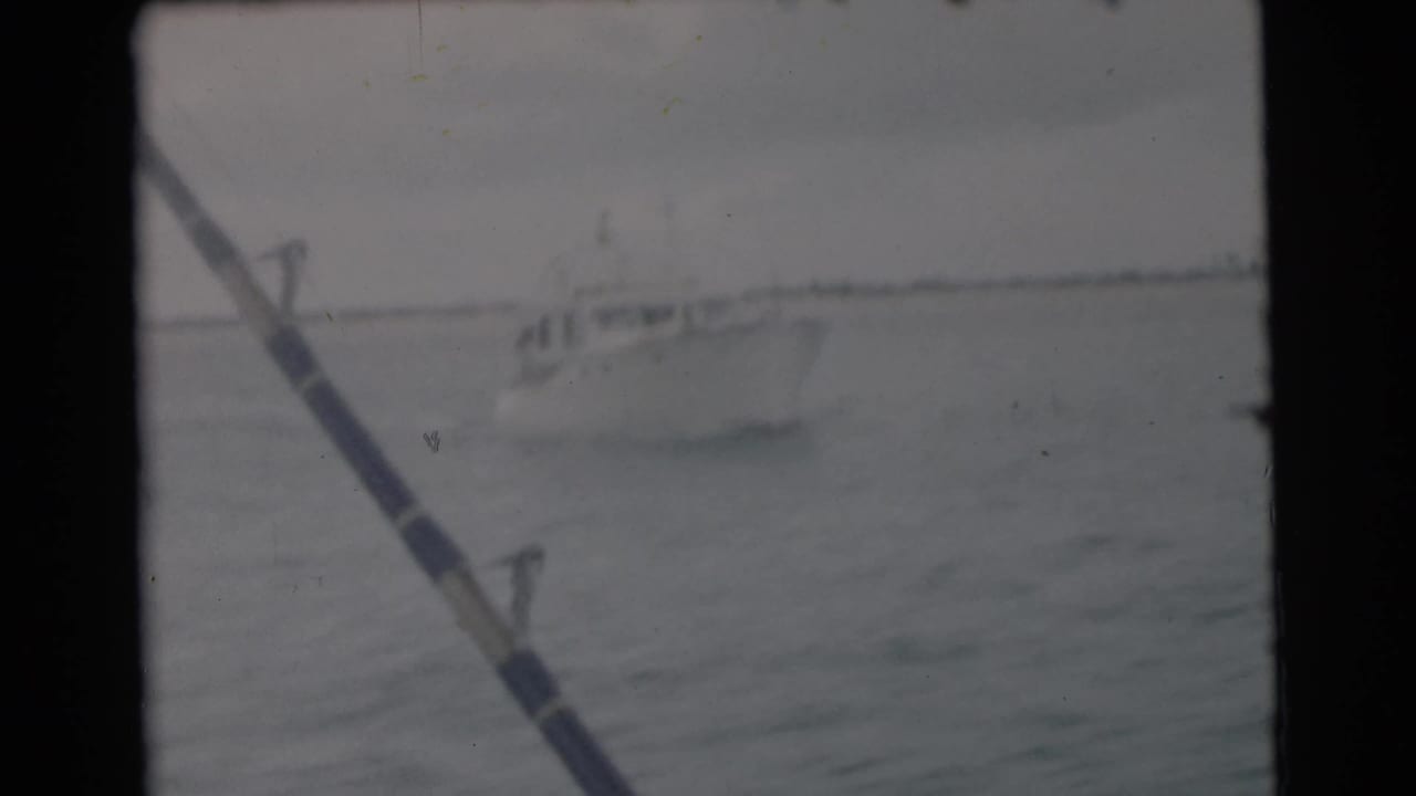 A white cabin boat appears on open water near Miami, partly framed by a fishing rod in this 1956 8mm home-movie still.