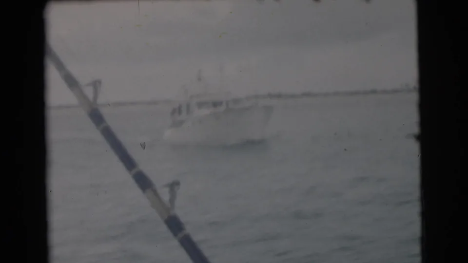 A white cabin boat appears on open water near Miami, partly framed by a fishing rod in this 1956 8mm home-movie still.