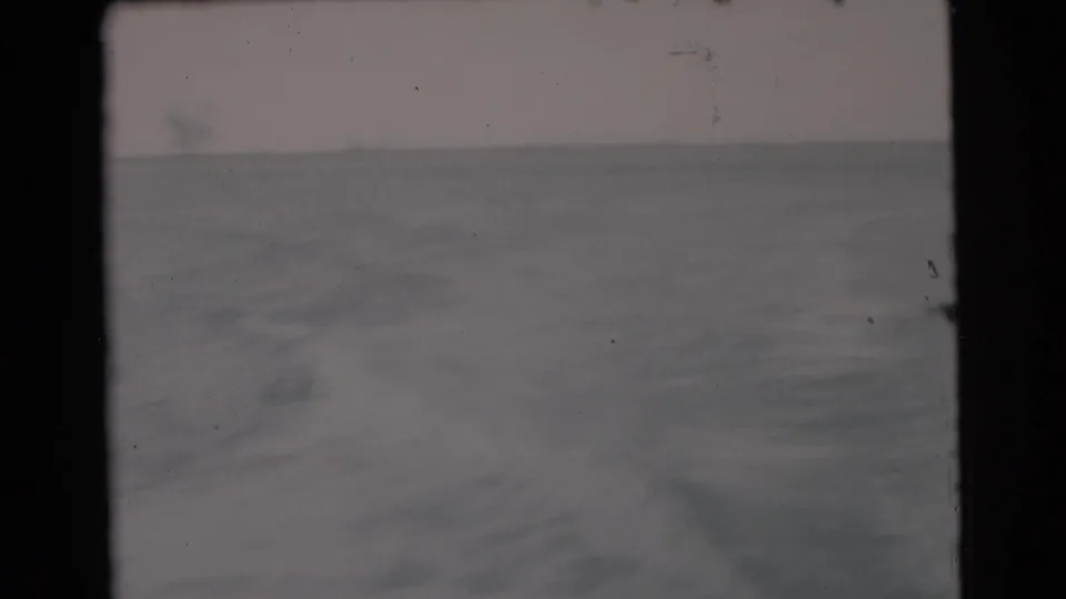 Soft 8mm frame from the boat's rear, showing churned wake, broad water surface, and a faint horizon near Miami in 1956.