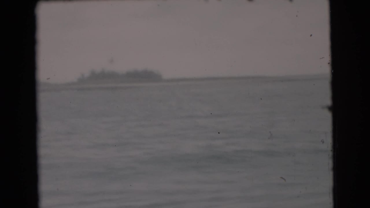 Distant low landform across calm water beneath a hazy sky.