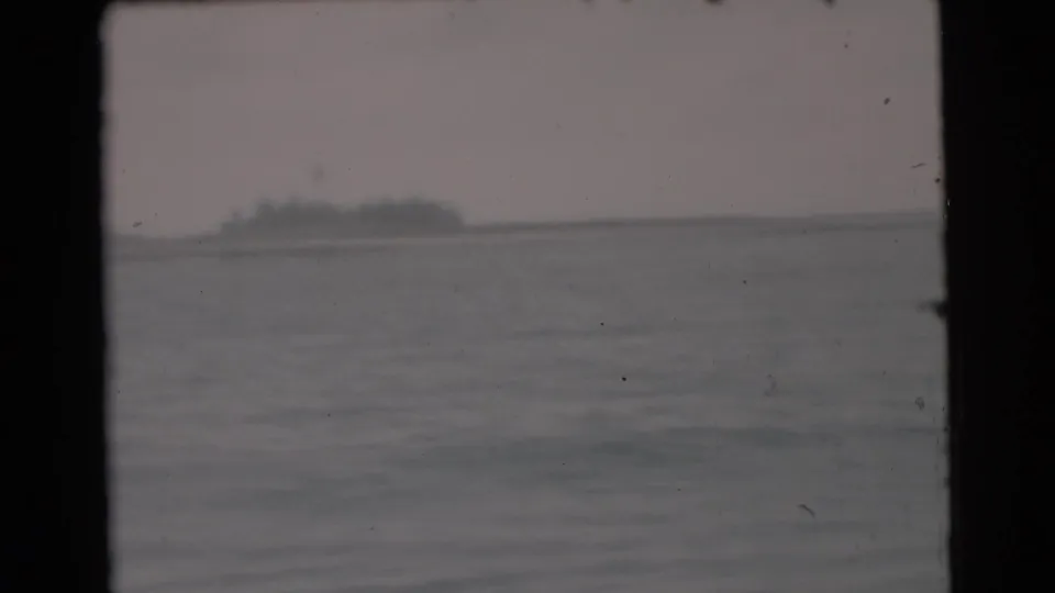 1956 Miami-area boating footage showing a distant low shoreline or island across calm water under a muted sky.