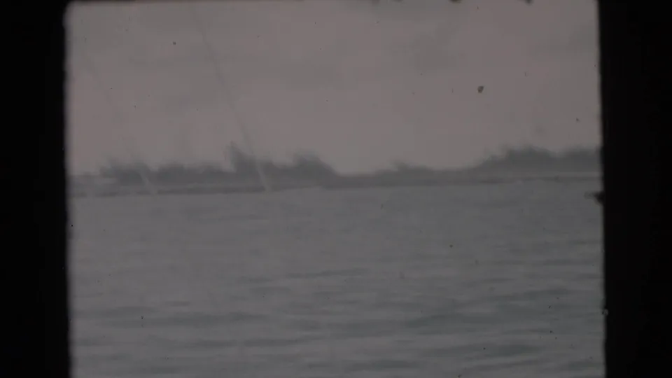 1956 Miami-area 8mm frame with low shoreline, open water, and faint diagonal boat or rigging lines in the foreground.