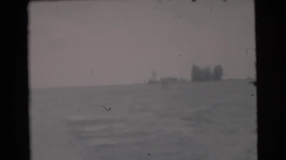 1956 Miami-area boating footage showing gray-blue water, overcast sky, and indistinct distant shoreline or structures.