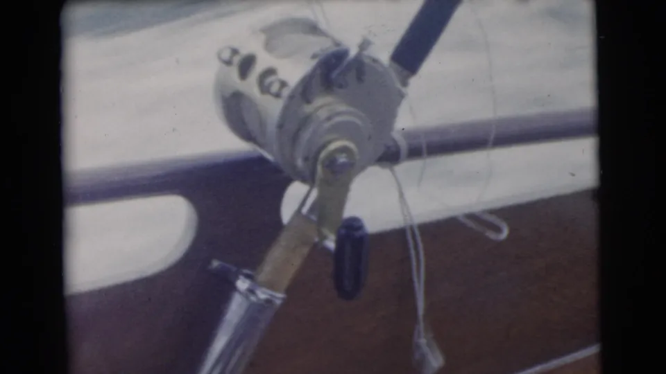 Close 1956 Miami-area 8mm view of a mounted fishing reel, rod handle, and boat rail during an ocean fishing trip.