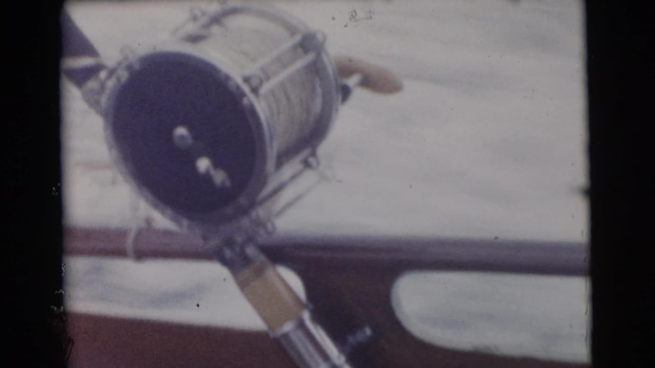 Close view of a large fishing reel and rod near a boat rail on open water.