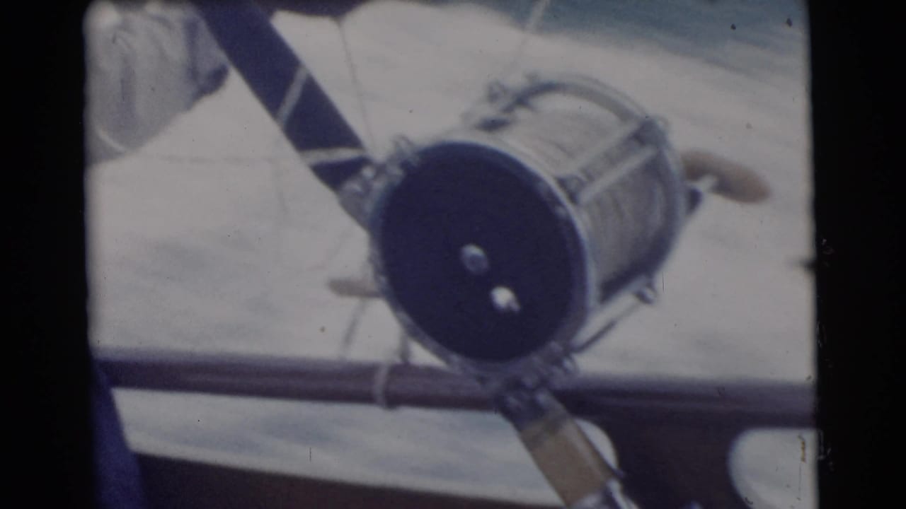 1956 Miami frame with the fishing reel and rod angled across the boat rail, suggesting a close home-movie view of the tackle.