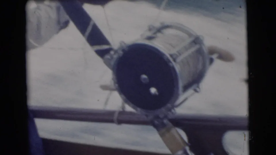 1956 Miami frame with the fishing reel and rod angled across the boat rail, suggesting a close home-movie view of the tackle.