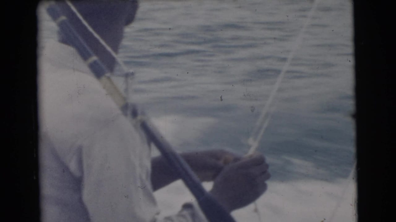 1956 Miami frame showing the man handling a taut fishing line near the rod, with calm water and the boat edge visible.