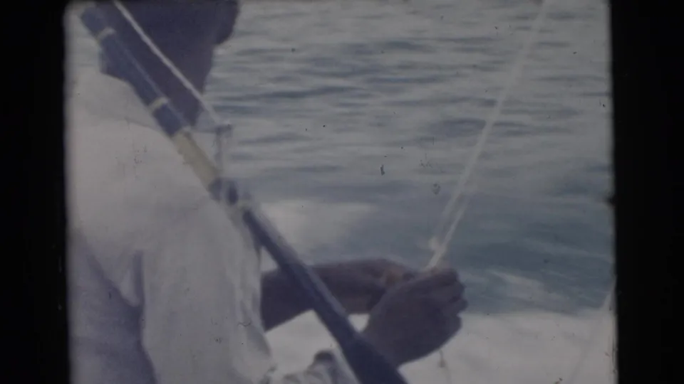 1956 Miami frame showing the man handling a taut fishing line near the rod, with calm water and the boat edge visible.