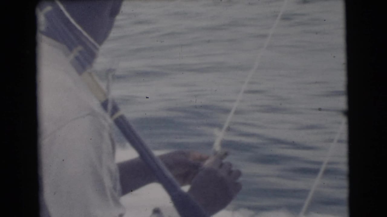 1956 Miami-area home-movie frame showing a man in a light shirt and cap handling a fishing rod from a boat on open water.