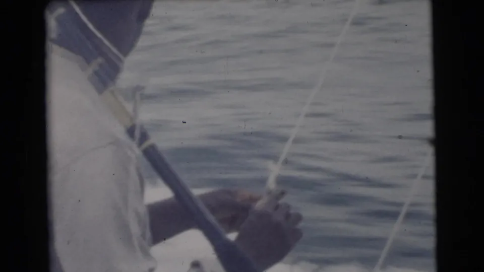 1956 Miami-area home-movie frame showing a man in a light shirt and cap handling a fishing rod from a boat on open water.