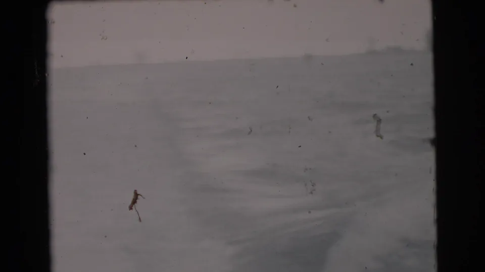 Vintage home-movie frame showing open water and distant haze, with soft exposure and visible dust marks.