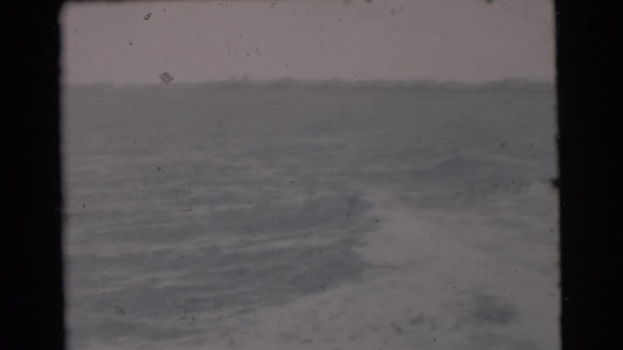Miami-area 1956 8mm frame showing open water through a dark boat or film-frame edge, with grain and muted color.