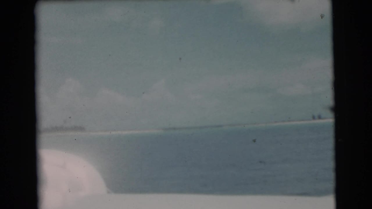 Calm water and distant shoreline seen from a boat under a cloudy sky.