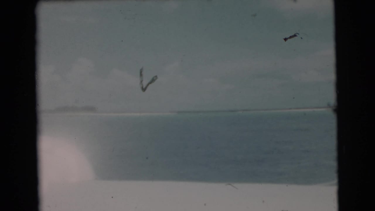 Faded 8mm frame from the Miami fishing scene, showing open water, low horizon, and a partial view of the fisherman at frame edge.