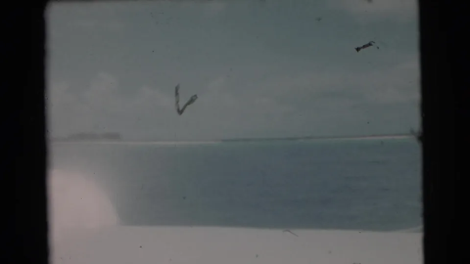 Faded 8mm frame from the Miami fishing scene, showing open water, low horizon, and a partial view of the fisherman at frame edge.