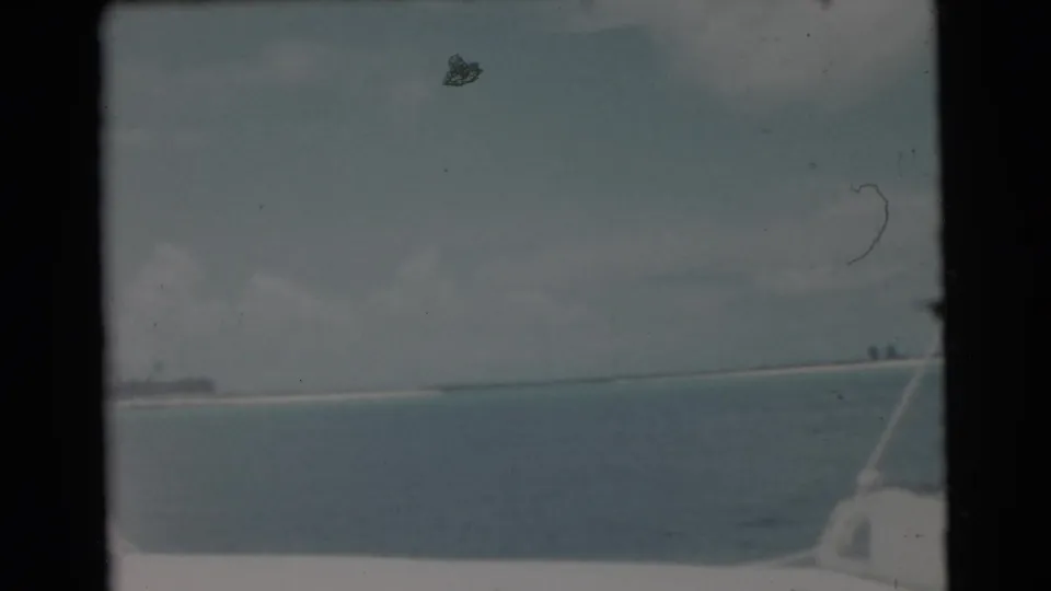 1956 Miami 8mm frame showing calm water, a low shoreline, cloudy sky, and a rod or boat line entering at the right edge.