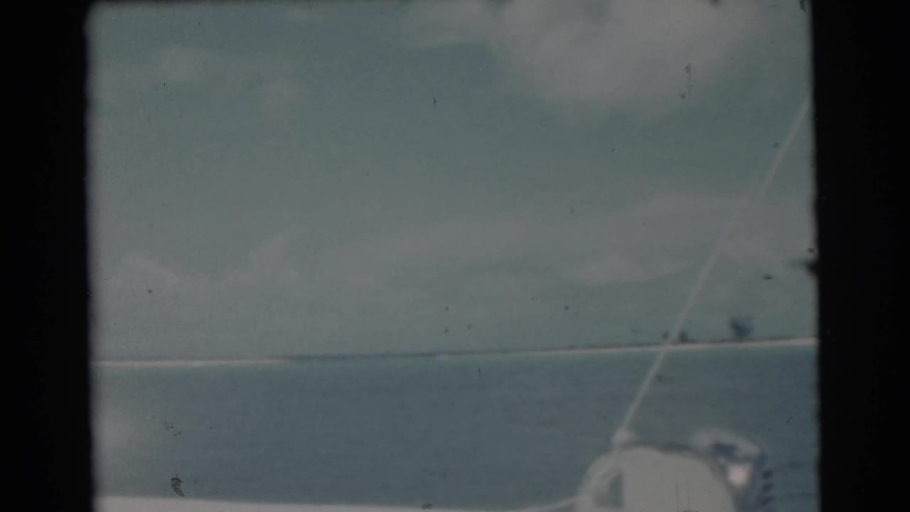 Boat rigging and edge in front of calm ocean and a distant low shoreline.