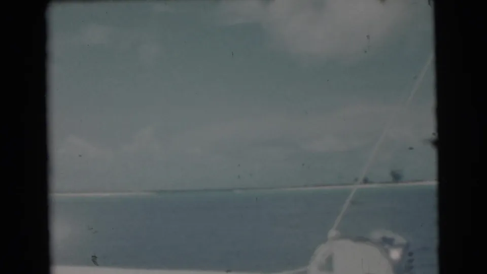 1956 8mm home-movie view from a boat near Miami, showing blue water, cloudy sky, rigging, and a faint shoreline.