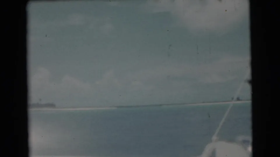 Faded 8mm frame of ocean seen from a boat, with rigging in the foreground and a distant shoreline under clouds.