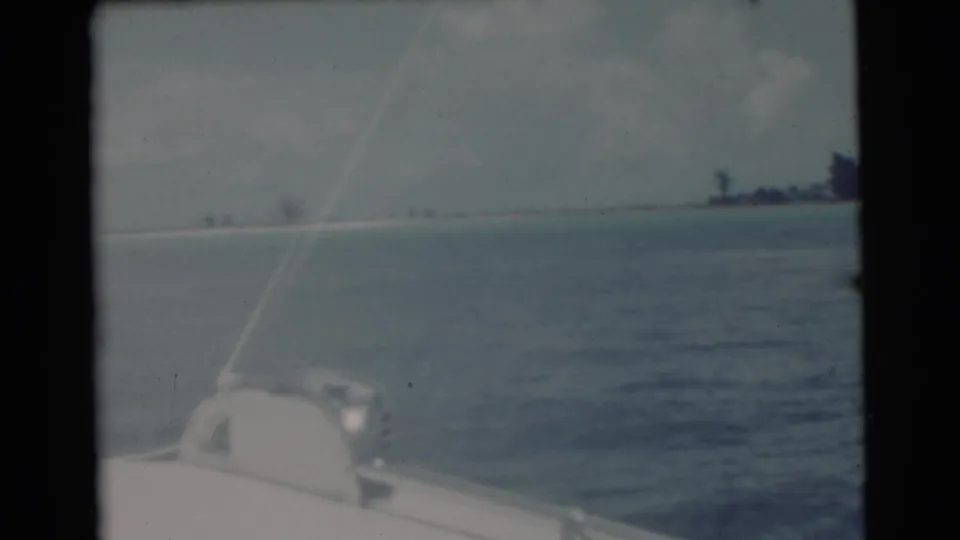 1956 coastal boat view near Miami with faded color, foreground boat hardware, rippled water, and tree shapes along the horizon.
