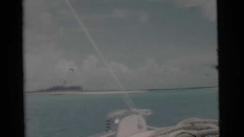 Faded 8mm Miami-area sailing view with rope, deck hardware, calm water, and a low tropical shoreline in the distance.