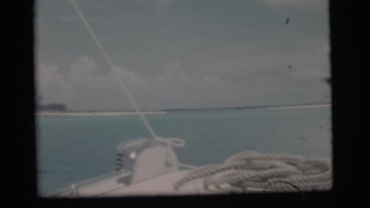 Boat deck with coiled rope looking across blue ocean toward a distant low island.