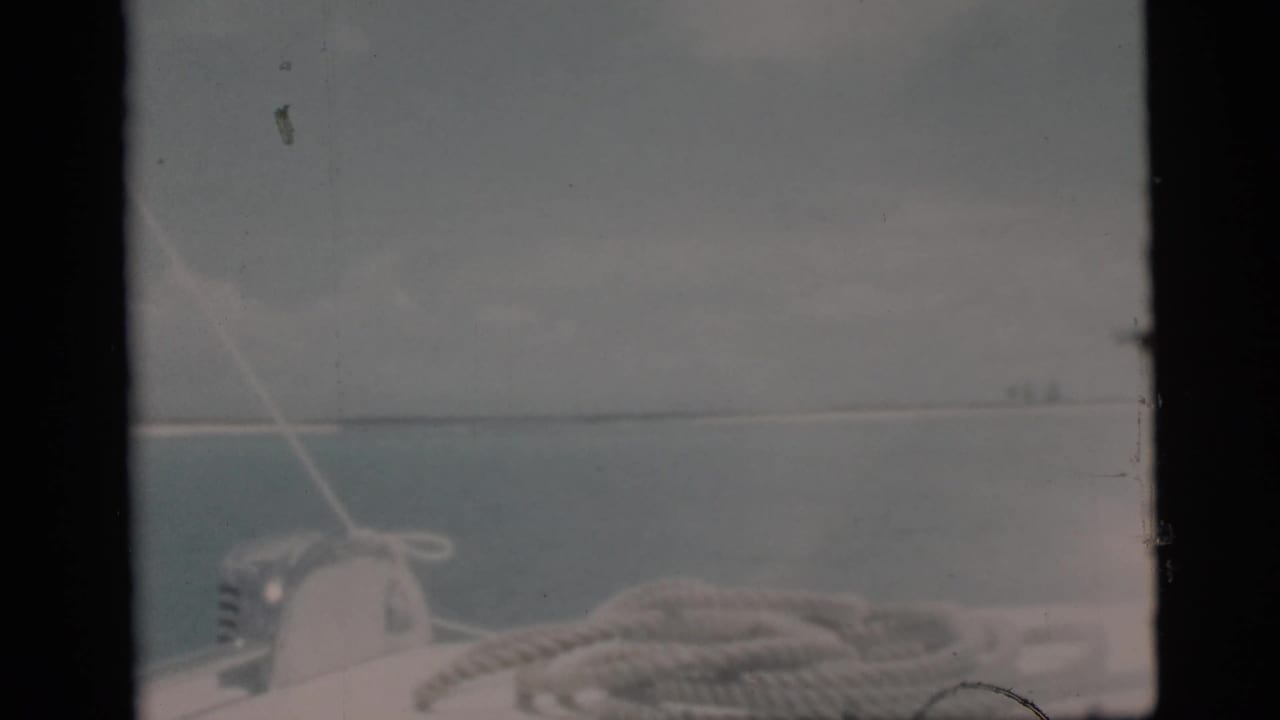 Blue ocean and distant shoreline seen past rope and a small deck fitting on a boat.